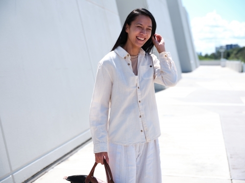 Asian woman wearing a white shirt and pants holding a black bag - Australian Stock Image