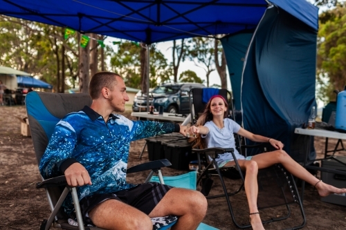 Aussie teenagers sitting with family in camp chairs at campground in Hunter Valley - Australian Stock Image