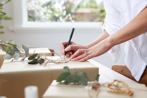 Close up of woman's hands writing gift tag for present - Australian Stock Image