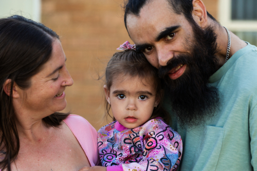 Australian parents with First Nations Australian toddler girl outside brick home - Australian Stock Image
