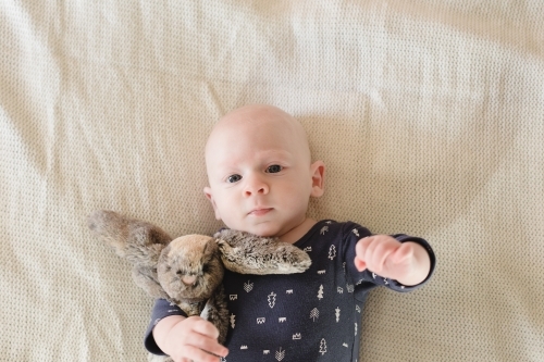 Baby boy cuddling a soft toy rabbit - Australian Stock Image