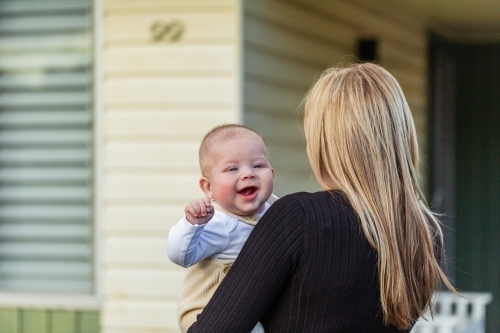 baby boy laughing over mothers shoulder outside family home - Australian Stock Image