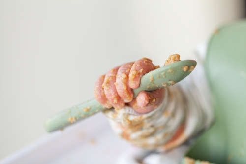 Baby hand covered in food holding spoon with copy space - Australian Stock Image