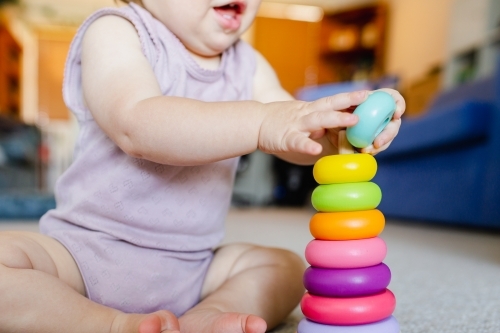 Baby learning through play developing fine motor skills with colourful stacking toy - Australian Stock Image