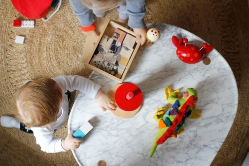 Baby playing with toys on marble coffee table and rug - Australian Stock Image