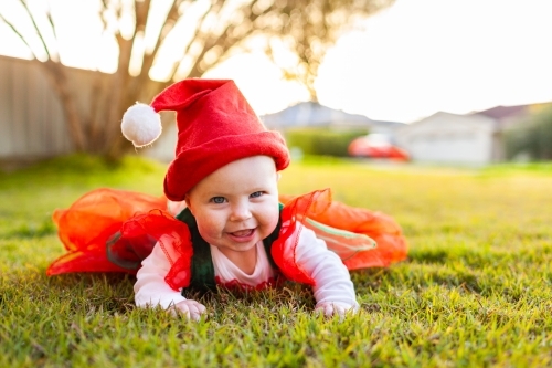 Baby ready for Christmas in red and greed outfit and Santa hat on grass - Australian Stock Image