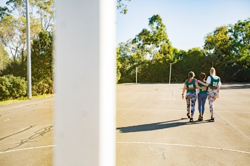 back shot of three young female athletes walking in a field on a sunny day with trees and clear sky - Australian Stock Image