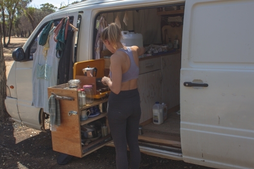 Backpacker girl enjoying vanlife, cooking on slide out kitchen with authentic van life clutter - Australian Stock Image