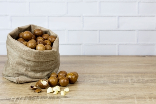Bag of macadamias on wooden bench, white brick background - Australian Stock Image