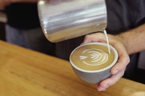 Barista pouring milk to make coffee art - Australian Stock Image