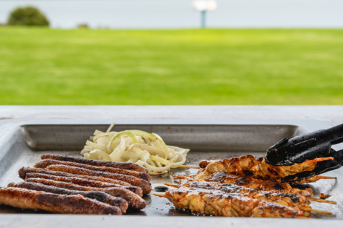 BBQ tray with grilled chicken, sausages, and caramelized onions cooking on it in park - Australian Stock Image