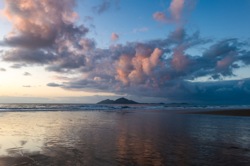 Beach scene at sunrise with waves and island - Australian Stock Image