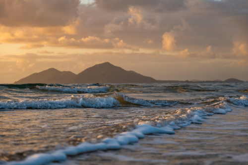 Beach scene at sunrise with waves and island - Australian Stock Image