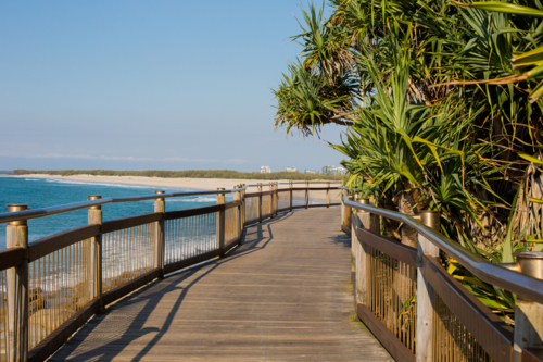 Beachside boardwalk curves along tropical coast. Empty path offers peaceful ocean views - Australian Stock Image