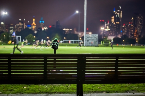 Bench seat at a sports ground with team training and city in background - Australian Stock Image