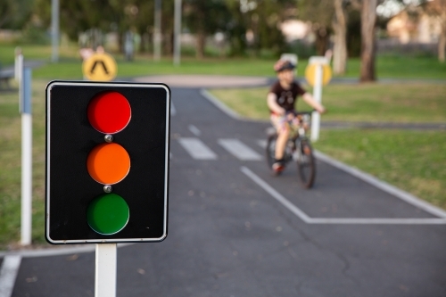 bike path with traffic signals and signs with a child riding a bike in the background - Australian Stock Image