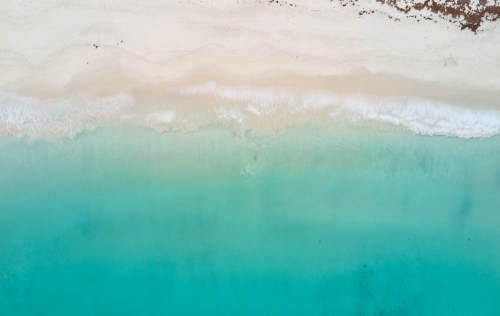 Bird's eye view of turquoise ocean waters lapping onto a sandy beach - Australian Stock Image