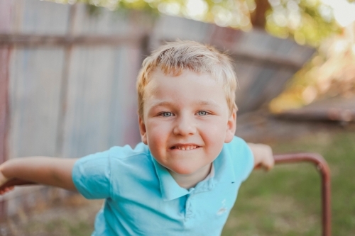 Blond blue eyed 5 year old boy sitting on outdoor bench - Australian Stock Image