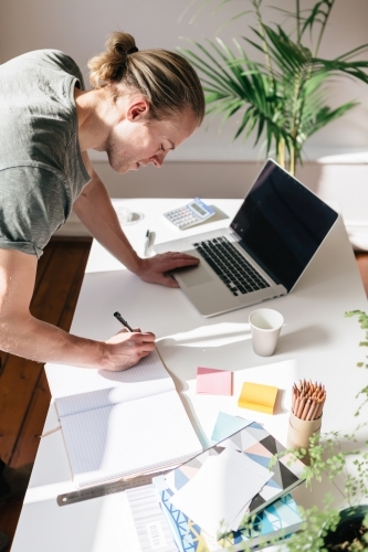 Blond young man writing in a notebook on a desk from above - Australian Stock Image