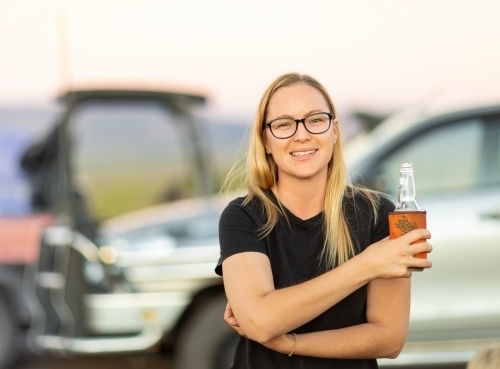 blonde bespectacled young woman outdoors holding beer bottle - Australian Stock Image