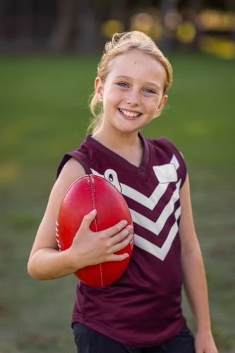 blonde girl holding red leather football and wearing football uniform