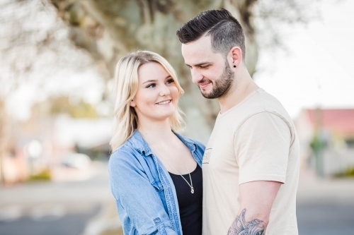 Blonde haired woman standing close looking at boyfriend with arm tattoo - Australian Stock Image