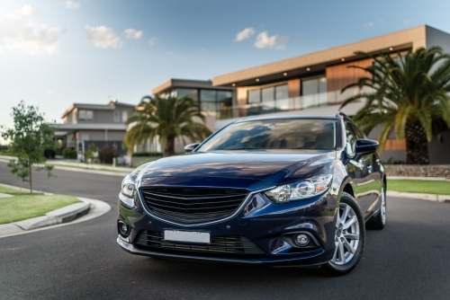 Blue station wagon on suburban street with luxury homes