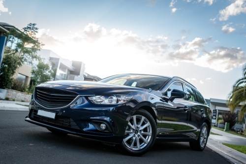 Blue station wagon on suburban street with luxury homes