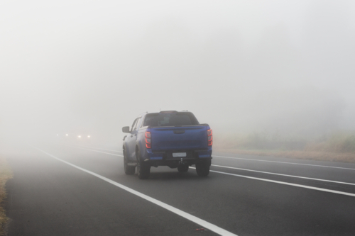 Blue ute travelling on highway road through fog with low visibility - Australian Stock Image