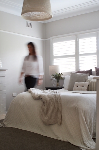 Blurred woman walking in bedroom with sunlit window - Australian Stock Image