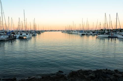 Boats and yachts moored either side of a channel in a marina in the early evening light - Australian Stock Image