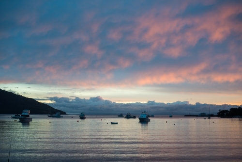 Boats in calm harbour water at sunset colourful sky and clouds - Australian Stock Image