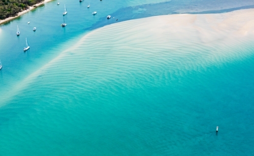 boats moored in a channel near patterned sand bar in blue water - Australian Stock Image