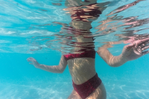 Body of woman in red bikini kneeling underwater in peaceful position with arms stretched out - Australian Stock Image