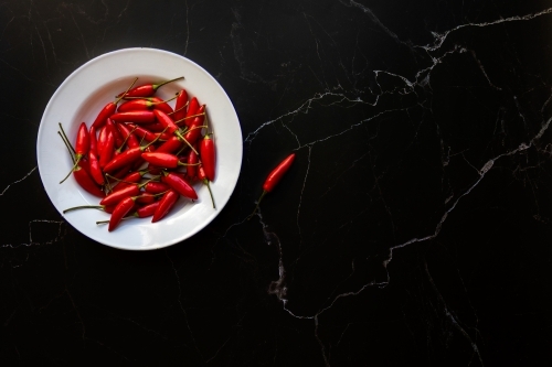 bowl of red chillies on black background - Australian Stock Image