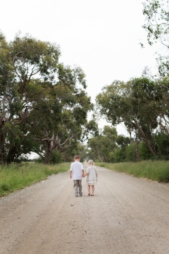 boy and girl holding hand walking down dirt road in the country - Australian Stock Image