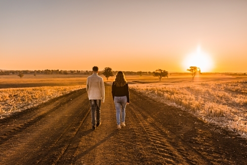 Boy and girl walking together on rural dirt road at sunset - Australian Stock Image