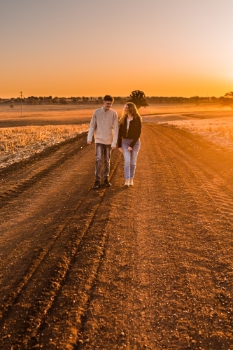 Boy and girl walking together on rural dirt road at sunset - Australian Stock Image