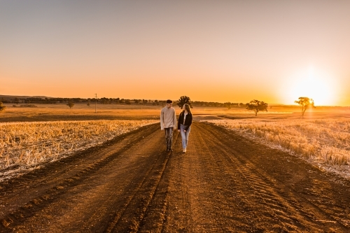 Boy and girl walking together on rural dirt road at sunset - Australian Stock Image