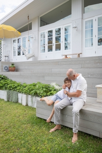 Boy and grandfather sitting together in backyard - Australian Stock Image