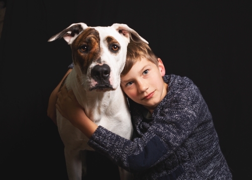 Boy and his dog studio portrait on black - Australian Stock Image