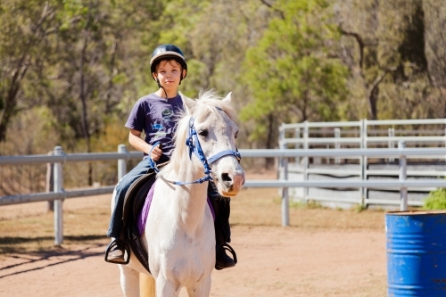 Boy child riding white pony during lesson - Australian Stock Image