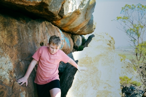 Boy climbing through rocks at on side of hill - Australian Stock Image