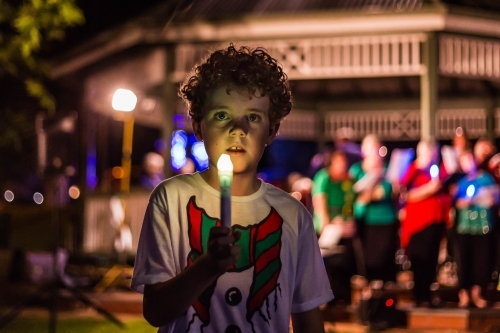 Boy holding candle at Christmas carols in the park at night time - Australian Stock Image