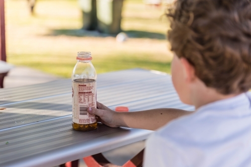 Boy holding drink container at park bench - Australian Stock Image