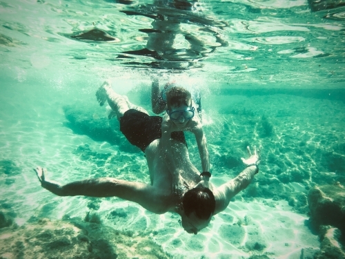 boy holding onto man diving underwater, taken underwater - Australian Stock Image