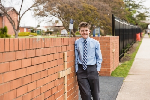 Boy in school uniform leaning on brick entrance with cross to private catholic school - Australian Stock Image