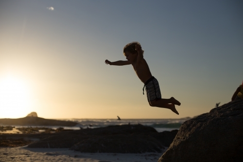 Boy jumping off a rock on the beach - Australian Stock Image