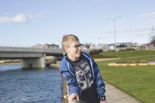 Boy leaning on fence near river - Australian Stock Image