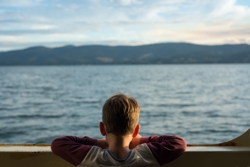 Boy looking above railling on ferry at the ocean - Australian Stock Image